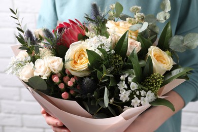 Photo of Woman with bouquet of beautiful roses near white brick wall, closeup