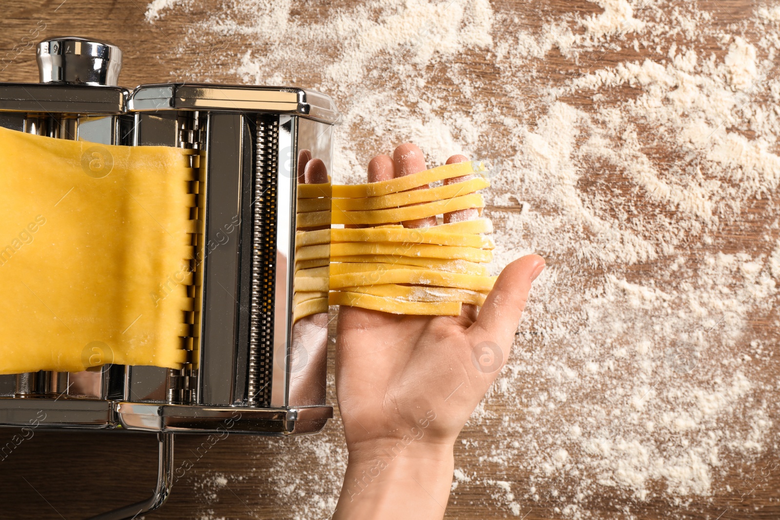 Photo of Woman preparing noodles with pasta maker machine at wooden table, top view