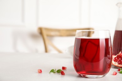 Photo of Glass of pomegranate juice and seeds on light table, space for text