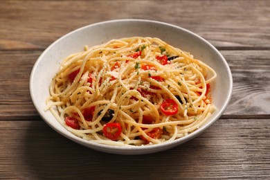 Photo of Bowl of delicious pasta with olives, tomatoes and parmesan cheese on wooden table