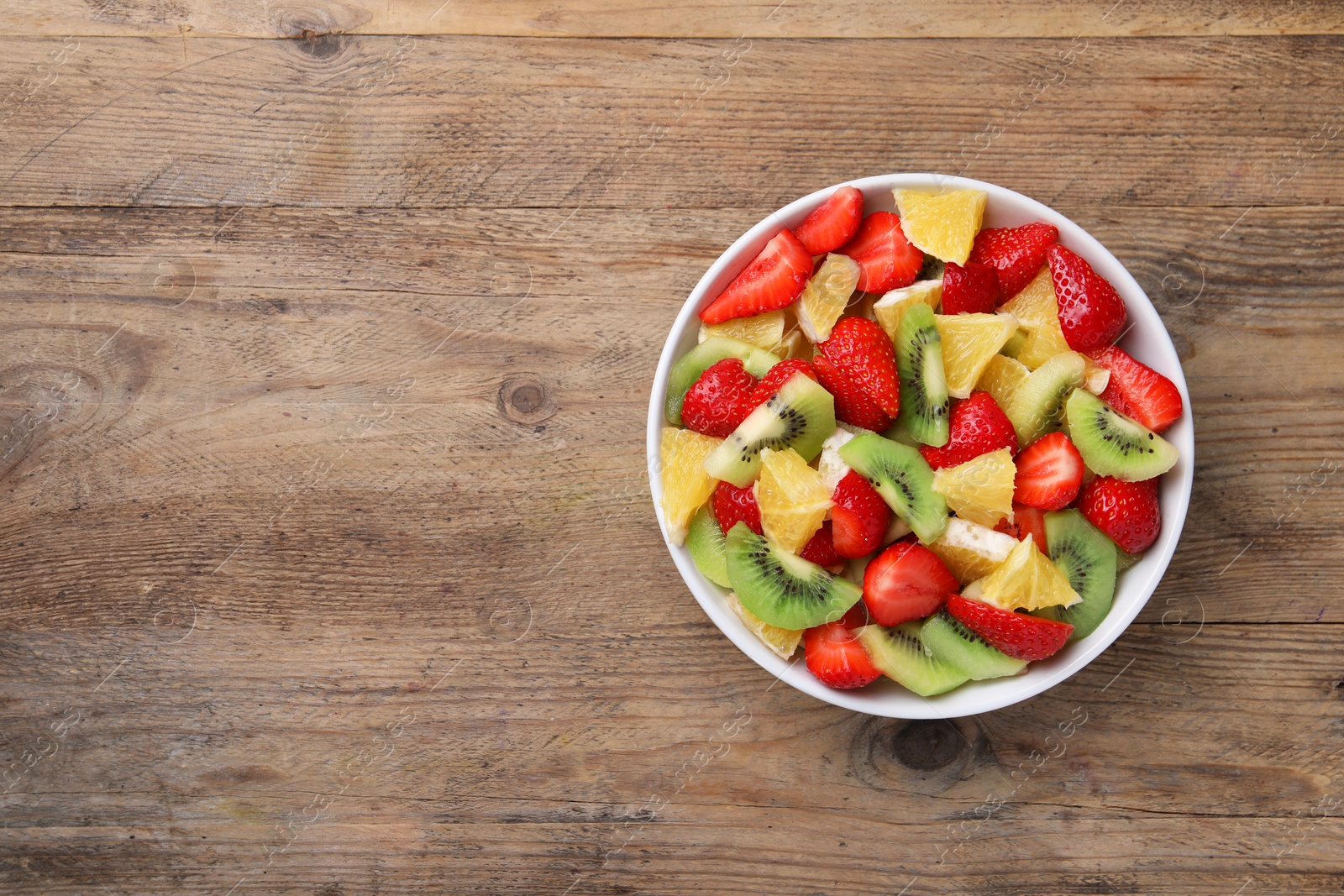 Photo of Delicious fresh fruit salad in bowl on wooden table, top view. Space for text