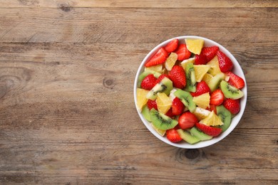 Delicious fresh fruit salad in bowl on wooden table, top view. Space for text