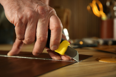 Man cutting leather with knife in workshop, closeup