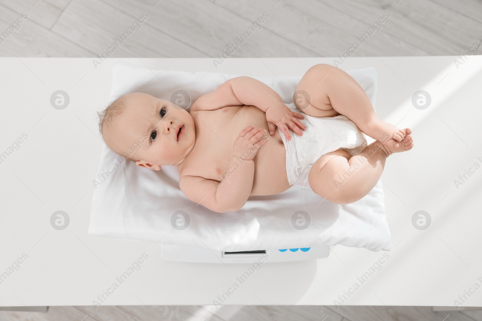 Photo of Cute little baby lying on scales in clinic, above view