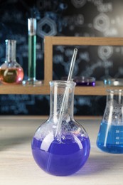 Laboratory glassware with blue liquid on white wooden table, space for text. Chemical reaction