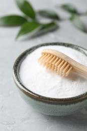 Bamboo toothbrush and bowl of baking soda on light gray table, closeup