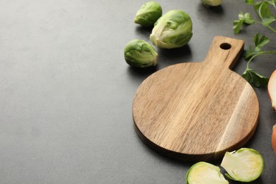 Photo of Wooden cutting board, Brussels sprouts and parsley on dark textured table, closeup. Space for text