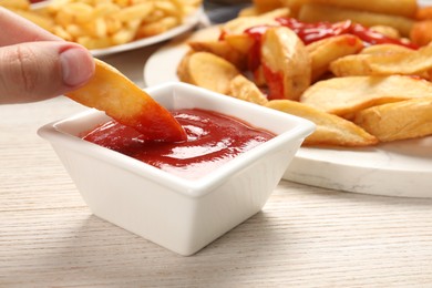 Photo of Woman dipping delicious baked potato wedge into bowl with ketchup at wooden table, closeup