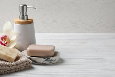 Photo of Soap bars, dispenser and terry towel on white wooden table. Space for text