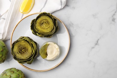 Delicious cooked artichokes with tasty sauce served on white marble table, flat lay. Space for text