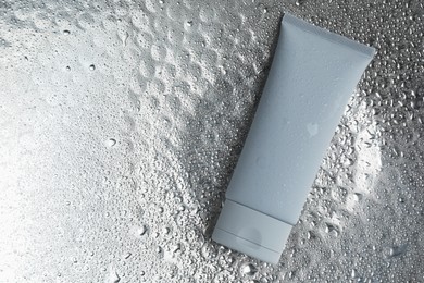 Photo of Moisturizing cream in tube on silver background with water drops, top view. Space for text