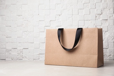 Photo of Paper shopping bag with ribbon handles on table near white wall. Mockup for design