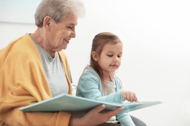 Photo of Cute girl and her grandmother reading book at home