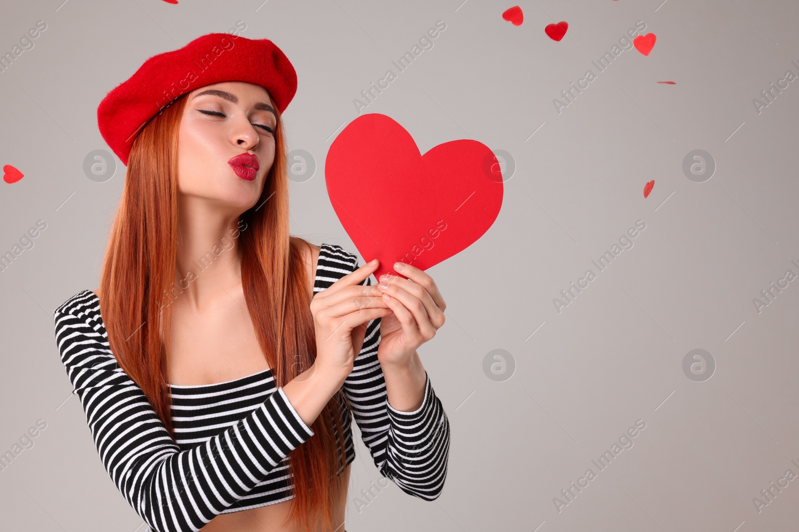 Photo of Young woman with paper heart under confetti on light grey background, space for text