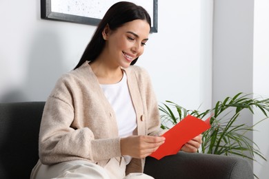 Photo of Happy woman reading greeting card on sofa in living room