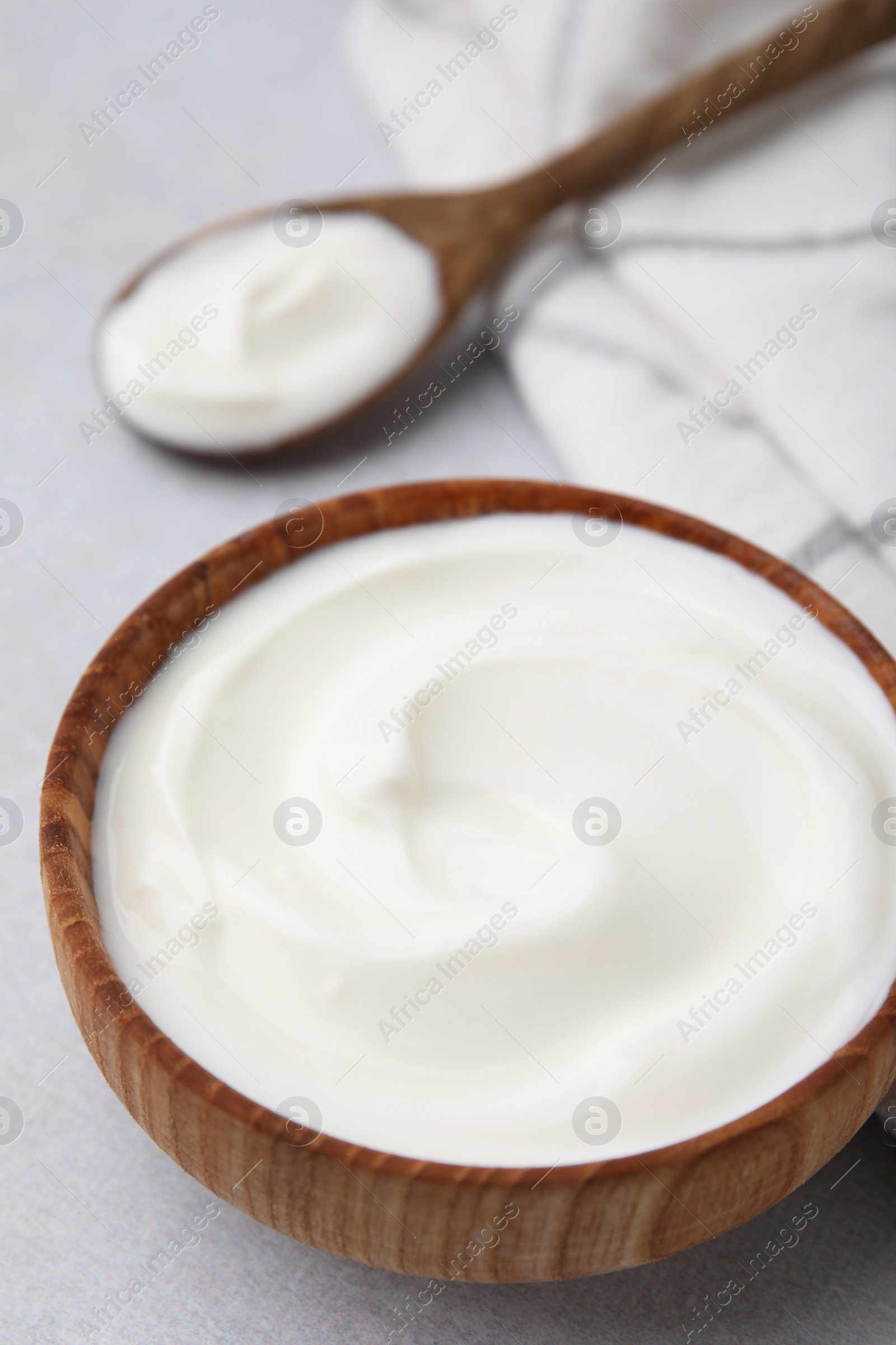 Photo of Delicious natural yogurt in bowl and spoon on light grey table, closeup