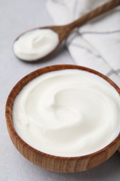 Delicious natural yogurt in bowl and spoon on light grey table, closeup