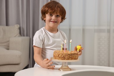 Photo of Birthday celebration. Cute boy with party blower at table with tasty cake indoors