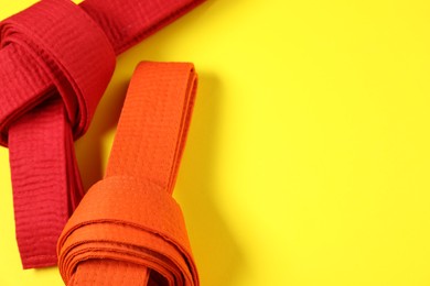 Photo of Red and orange karate belts on yellow background, flat lay. Space for text