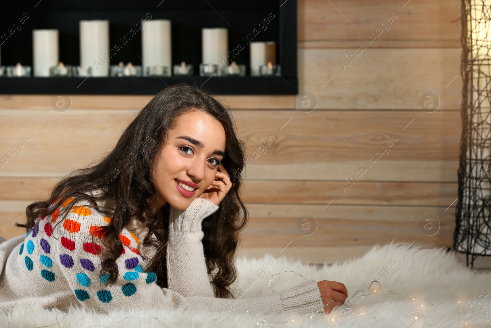 Photo of Portrait of young beautiful woman in warm sweater lying on rug at home