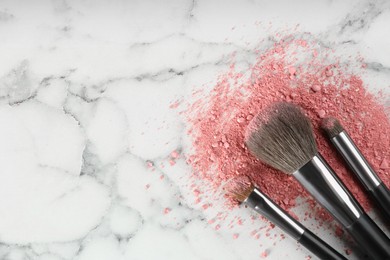 Makeup brushes and scattered blush on white marble table, flat lay. Space for text