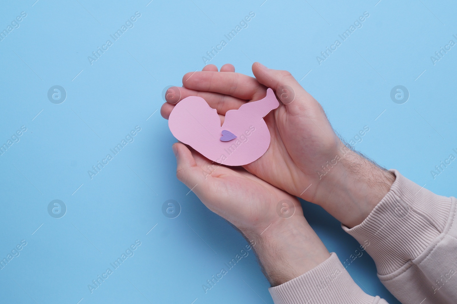 Photo of Female health. Woman holding newborn paper figure on light blue background, top view with space for text