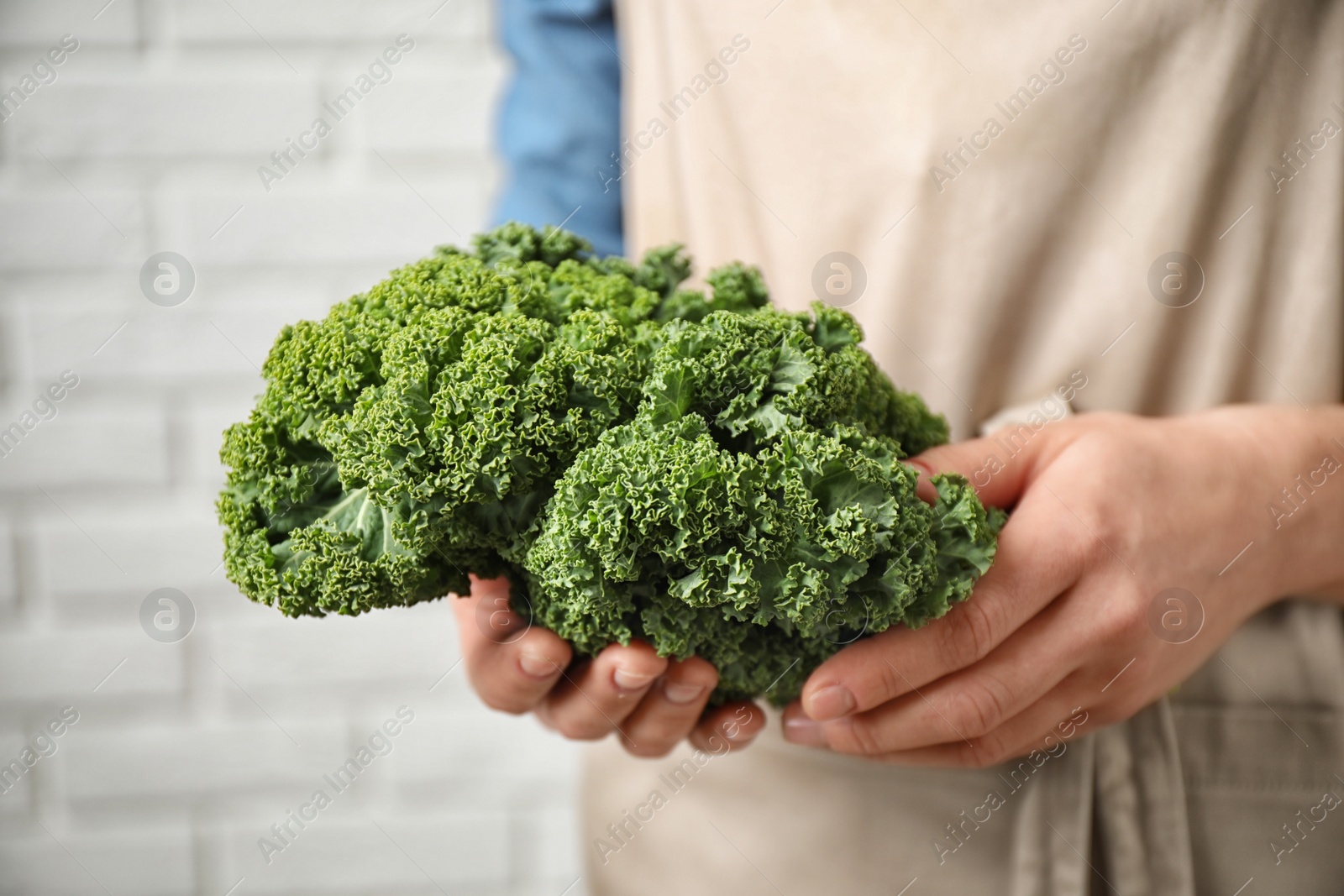 Photo of Woman holding fresh kale leaves near white brick wall, closeup