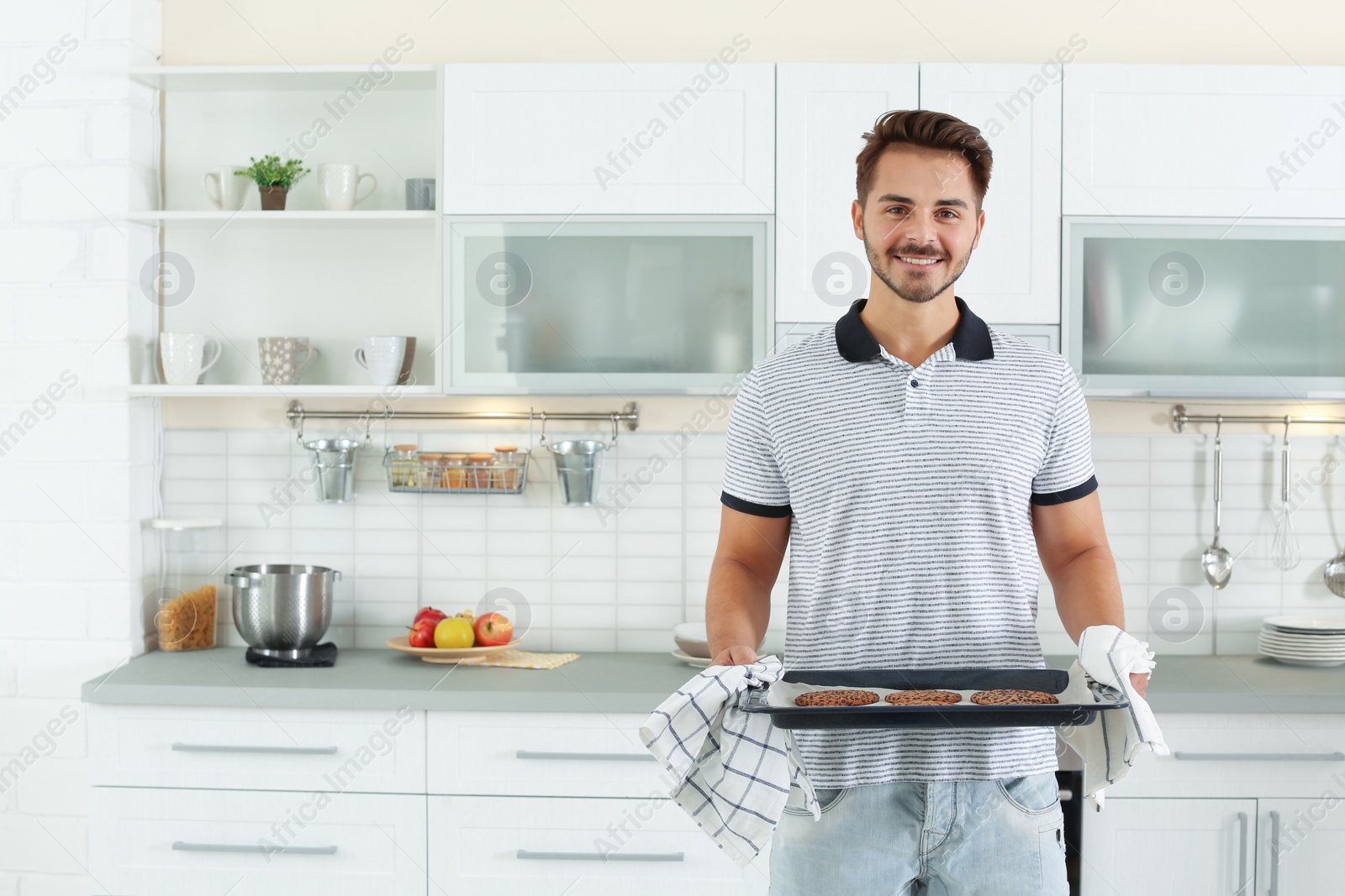 Photo of Young man holding oven sheet with cookies in kitchen, space for text