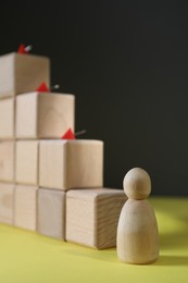 Photo of Stairs of cubes with pins as barrier and wooden human figure on yellow surface, space for text. Path to growth and success