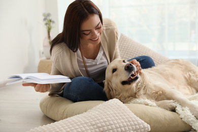 Photo of Young woman with book and her Golden Retriever at home. Adorable pet