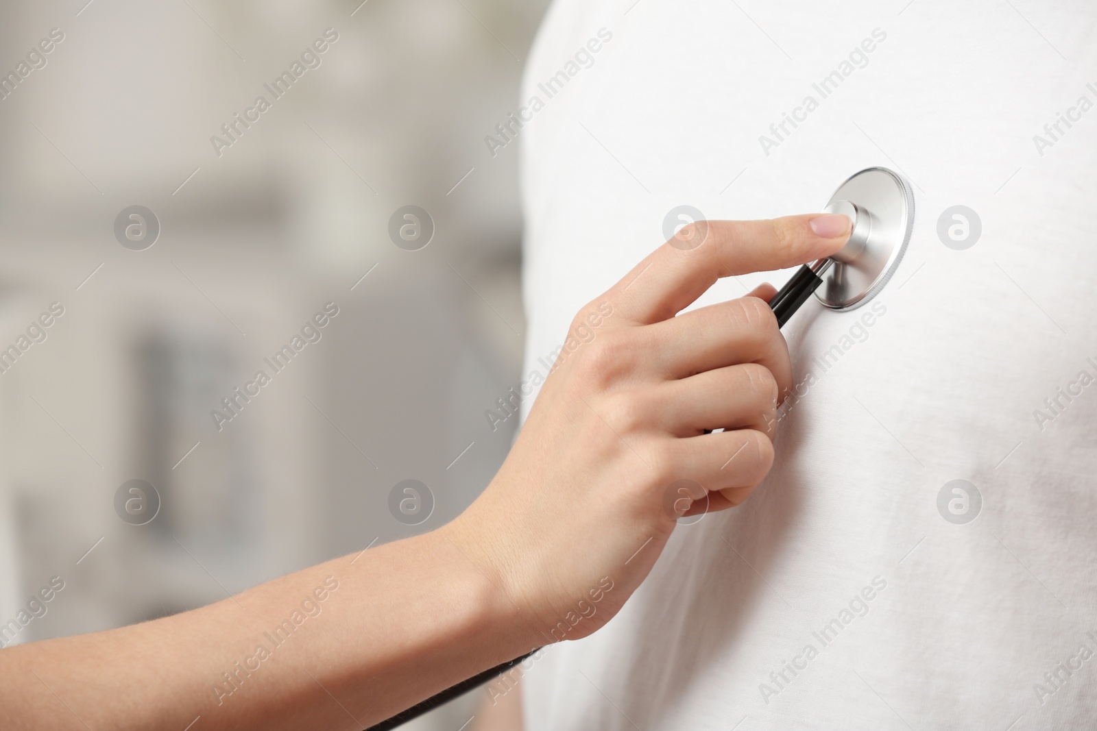 Photo of Doctor examining patient with stethoscope against blurred background, closeup