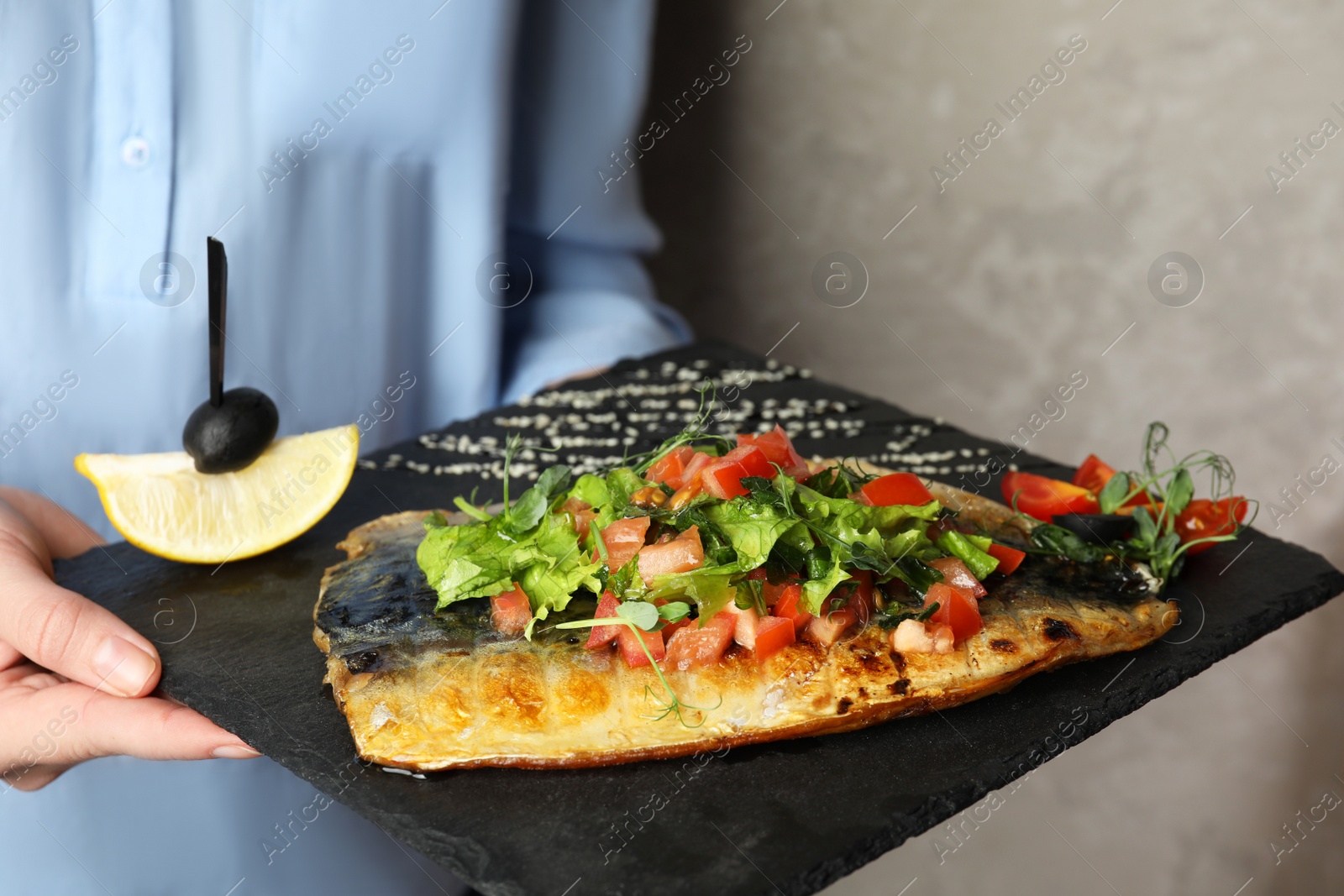 Photo of Woman holding slate plate with delicious grilled fish on grey background, closeup