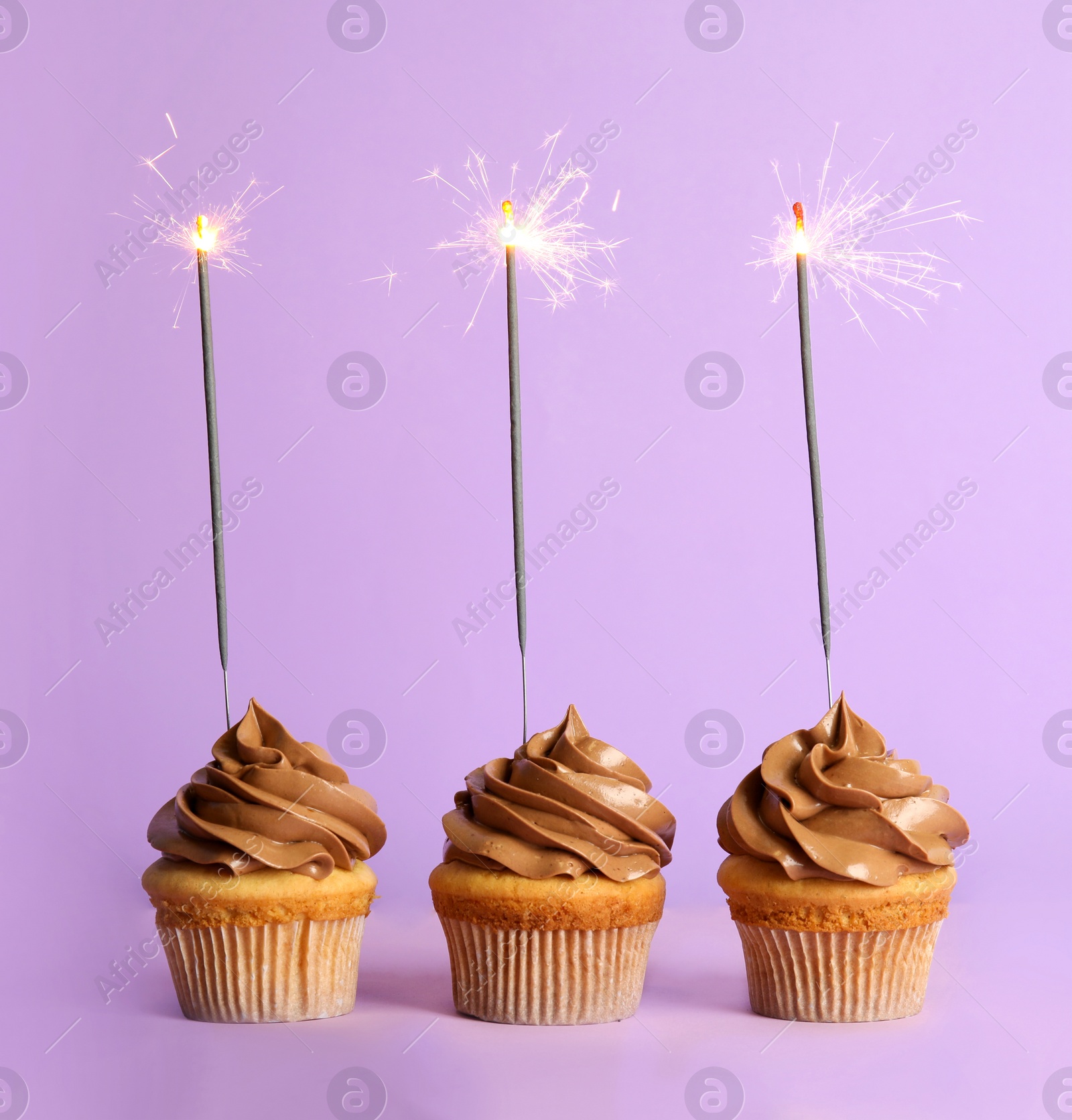Photo of Birthday cupcakes with sparklers on violet background