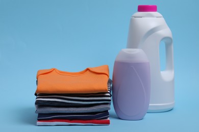 Photo of Stack of baby clothes and laundry detergents on light blue background