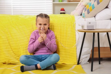 Photo of Little girl using nebulizer for inhalation on floor at home