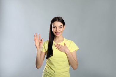 Attractive young woman showing hello gesture on grey background