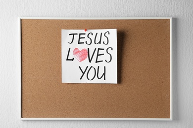 Photo of Cork board with paper and written text JESUS LOVES YOU on white background