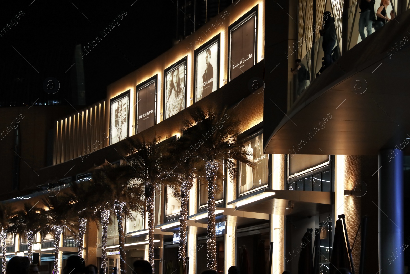 Photo of DUBAI, UNITED ARAB EMIRATES - NOVEMBER 04, 2018: Illuminated building and palms decorated with garlands on city street