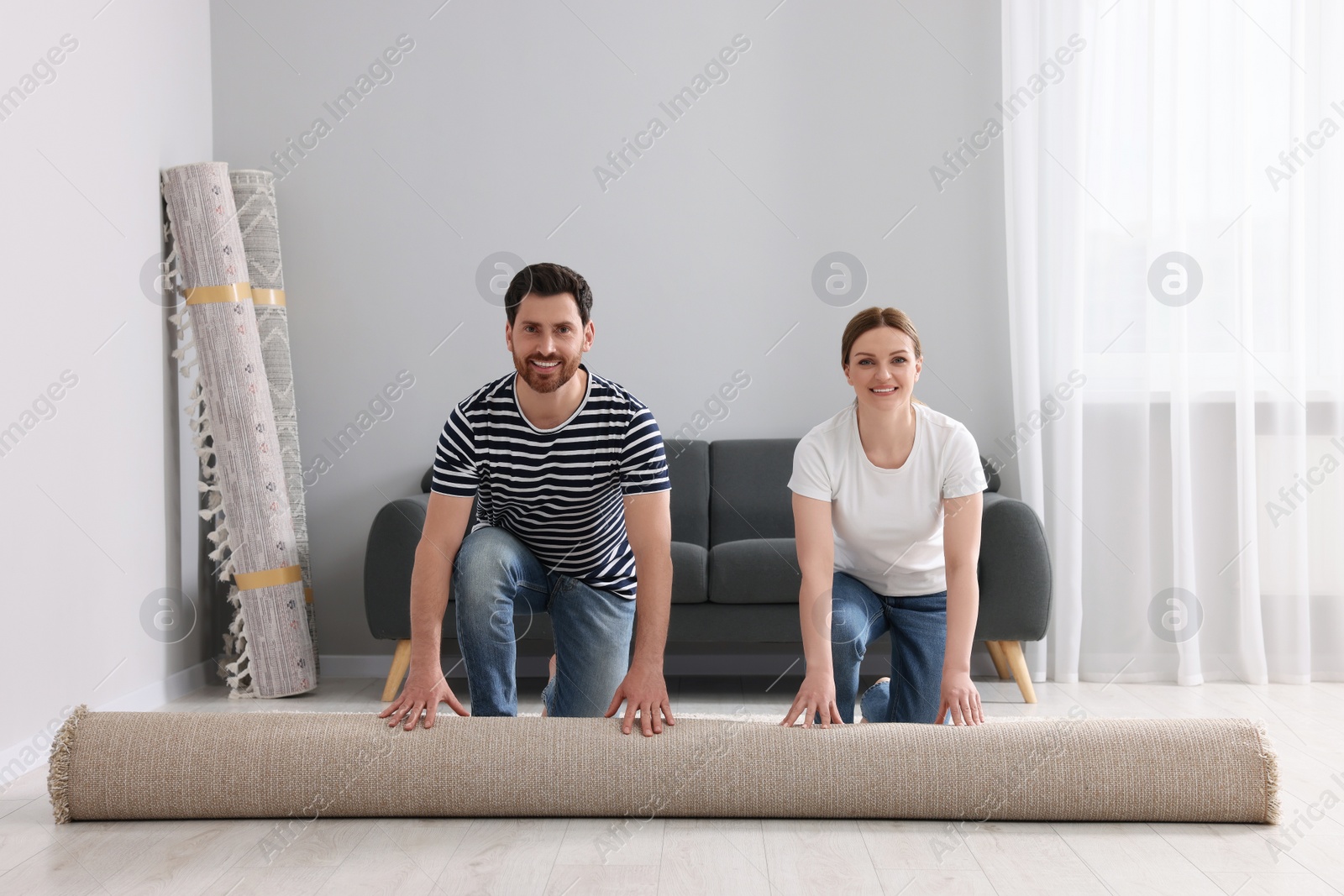 Photo of Smiling couple unrolling carpet on floor in room