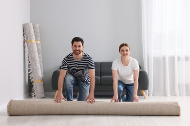 Photo of Smiling couple unrolling carpet on floor in room