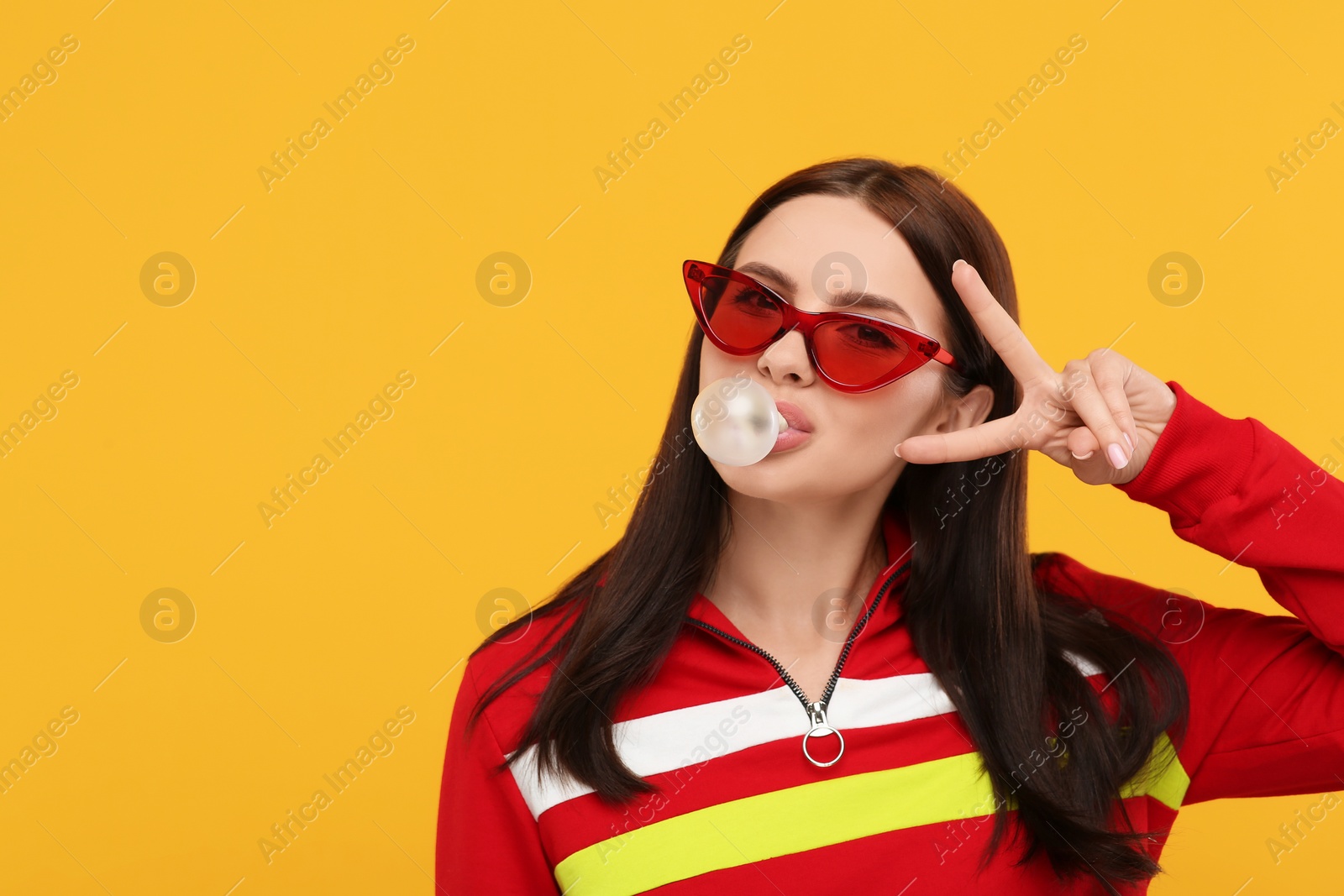 Photo of Beautiful woman blowing bubble gum and gesturing on orange background, space for text