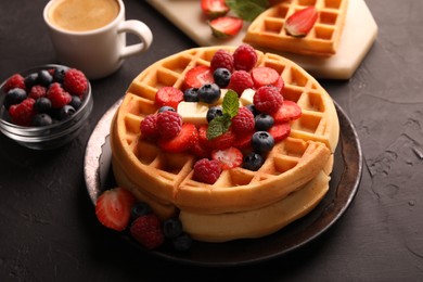 Tasty Belgian waffles with fresh berries, cheese and cup of coffee on black table, closeup