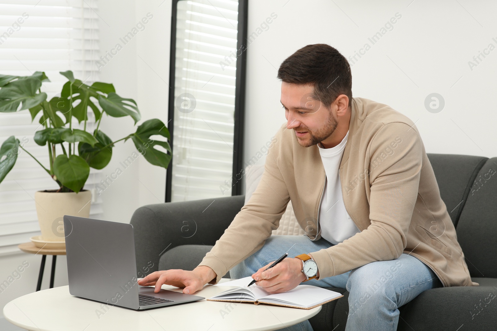 Photo of Man working with laptop at table in living room