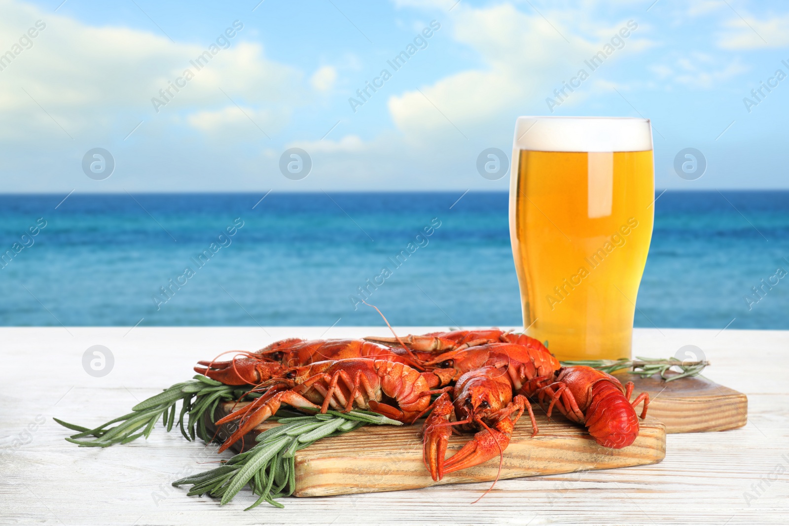 Image of Cooked crayfishes served with beer on white wooden table near sea