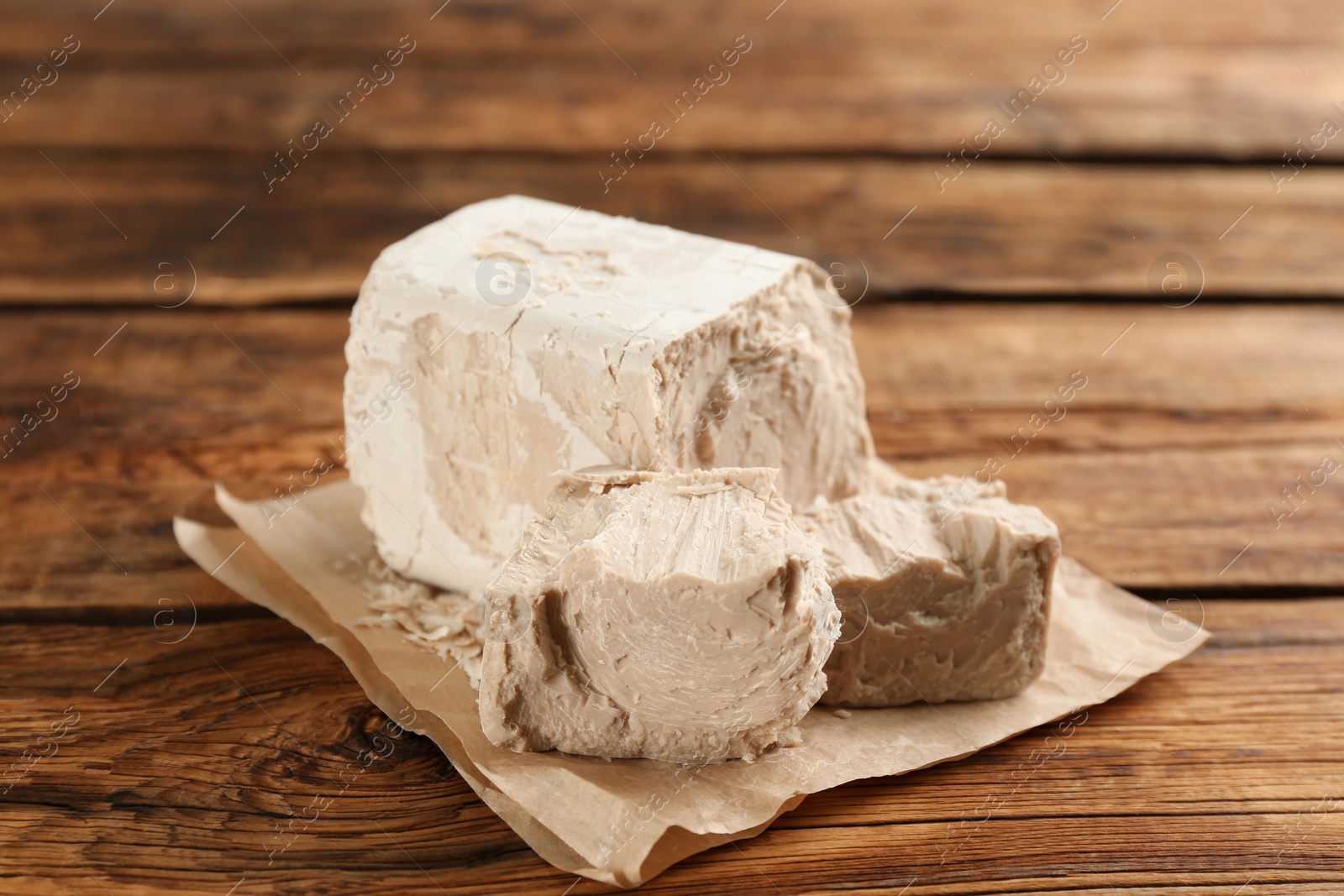 Photo of Pieces of compressed yeast with parchment on wooden table, closeup