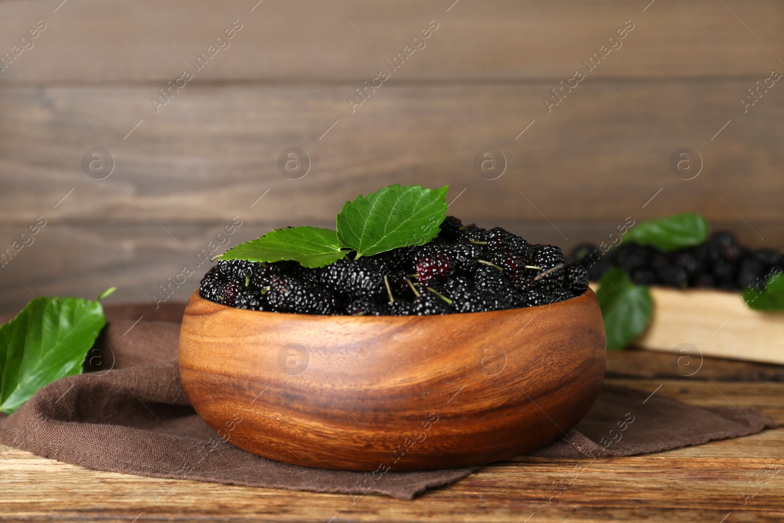 Photo of Fresh ripe black mulberries and leaves in bowl on wooden table