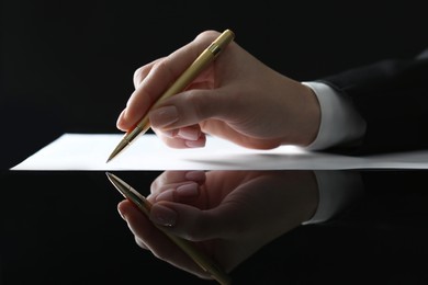 Woman writing on sheet of paper at glass table, closeup