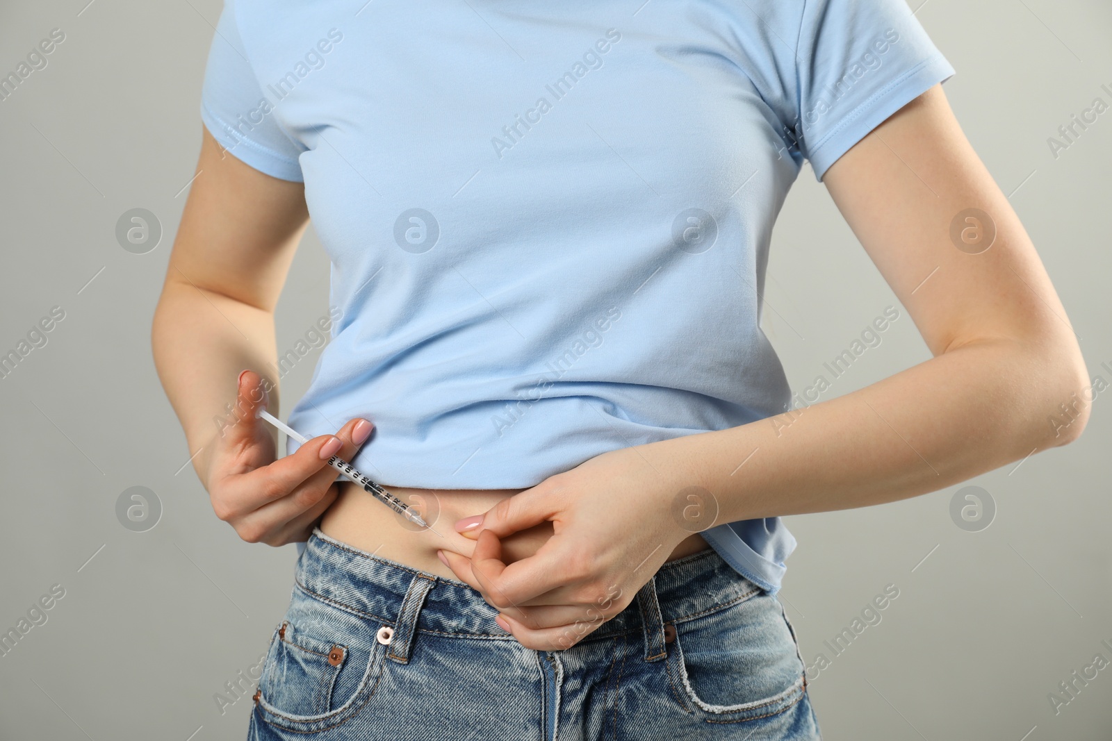 Photo of Diabetes. Woman making insulin injection into her belly on grey background, closeup