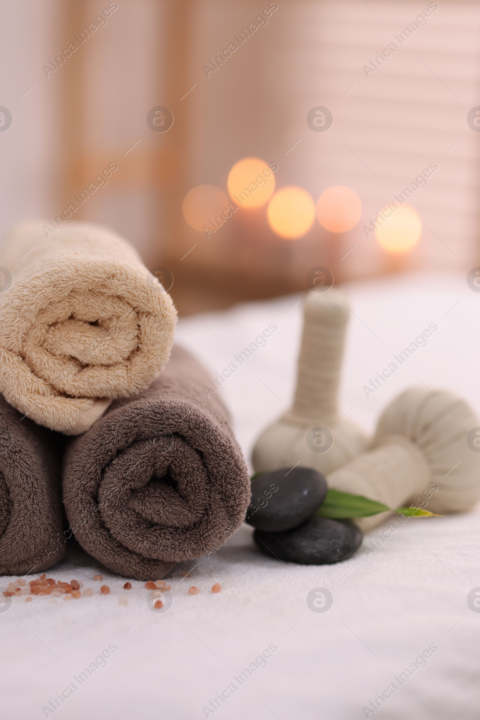 Photo of Spa stones, rolled towels and herbal bags on massage table indoors, closeup