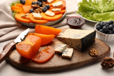 Photo of Tasty sliced persimmon and blue cheese on wooden board, closeup